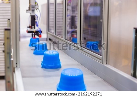 Blue polypropylene pots on conveyor belt of automatic plastic injection molding machine with robotic arm at exhibition, trade show. Manufacturing, industry and automated technology equipment concept