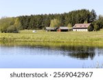 A blue pond with green fields, trees and a farmhouse in the distance