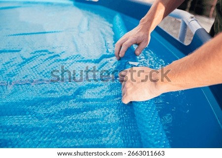 The blue pool cover is assembled into a roll by men's hands, the concept of summer recreation and pool maintenance.