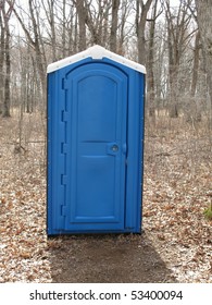 A Blue Porta Potty Toilet Outhouse In A Woods.