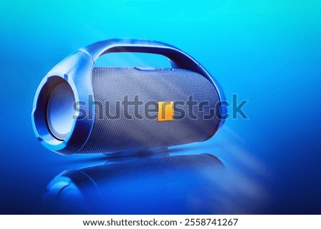 Blue portable wireless Bluetooth speaker, with reflection on a blue gradient background. Device for playing music. Music background.