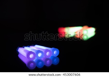 Blue and purple glowsticks in a row on a reflective surface with other colours in the background