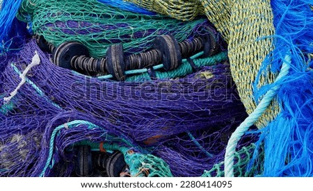 Blue, purple, green and yellow trawling nets stacked on the dockside next to fishing trawlers waiting for the next tide.