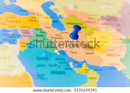 Blue push pin pointing at Iran on a political world map