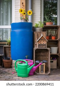 A Blue Rain Barrel With Two Watering Cans In The Garden, Harvesting Rainwater To Reuse It