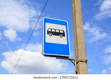 Blue rectangular bus stop sign on an old metal pole. Black silhouette of a bus on a white background symbolizes the passenger boarding area. Traffic regulations, road safety concept.