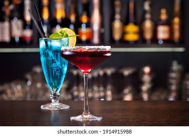 Blue and red cocktails on the bar. Alcoholic cocktails on a background of shelves with bottles. Blurred bottles of alcohol on the wall of the bar. - Powered by Shutterstock