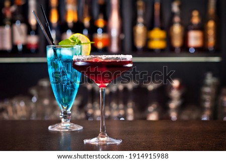 Blue and red cocktails on the bar. Alcoholic cocktails on a background of shelves with bottles. Blurred bottles of alcohol on the wall of the bar.