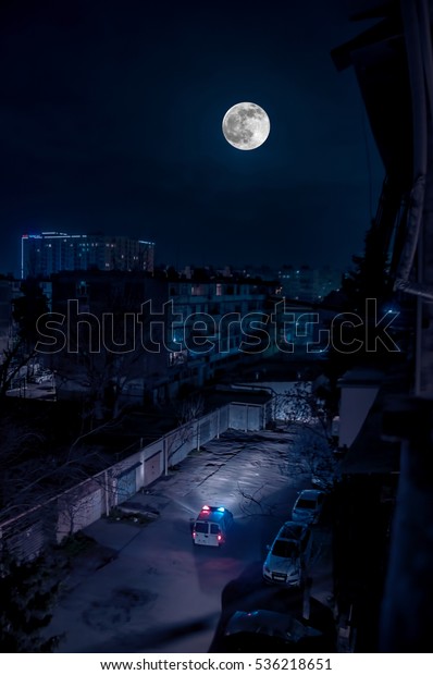 Blue and red  light flasher atop of a
police car in the yard at night with full
moon
