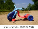 Blue and red used toddler tricycle big wheel bike sitting outside. 