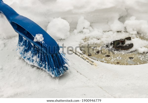 Blue removal brush removes snow from the\
airplane wing near the gas station neck on a winter day, snowfall,\
non-flying weather,\
close-up.