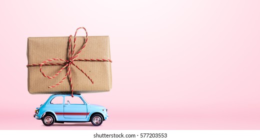 Blue retro toy car delivering gift box for Valentine's day on pink background