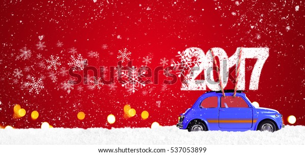 Blue retro toy car delivering Christmas or New\
Year 2017 on festive red\
background