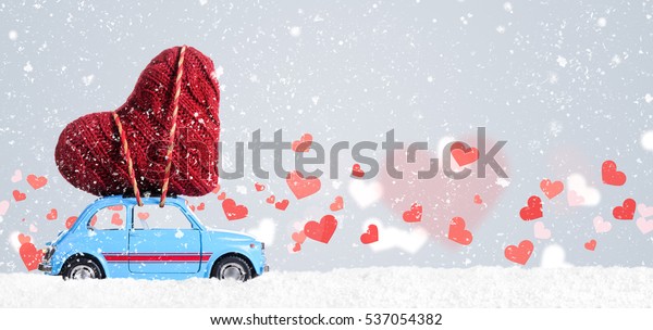Blue retro toy car delivering heart for\
Valentine\'s day on gray\
background