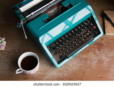 blue retro typewriter sitting on wooden coffee table and cup of coffee, and notepad are good for authors, writers, editors or journalists