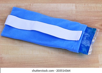 Blue Reusable Soft Gel Filled Cold And Hot Pack To Relieve Pain Inside A Fabric Pouch, On Wooden Background