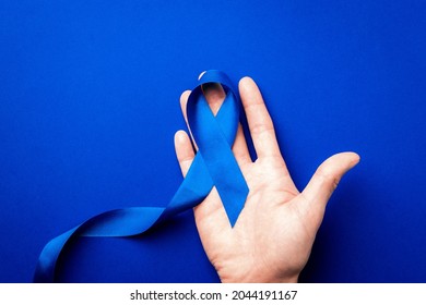 Blue ribbon. Awareness prostate cancer of men health in November. Blue ribbon in hands isolated on deep blue background. Symbol of oncology affected man. Copy space
