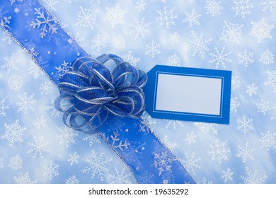 Blue Ribbon And Blank Gift Tag On Snowflake Background With Bow Making A Present