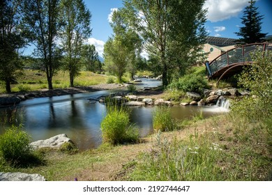 The Blue River Flowing Through Steamboat Springs.  Green Bushes And Trees Along With Blue Water. Reflection Of Trees On Calm Water.