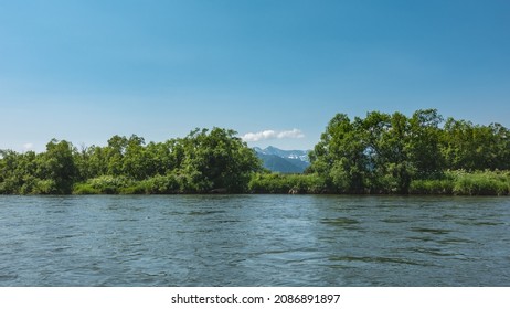 The Blue River Flows Calmly. Ripples On The Water. There Is Lush Green Vegetation On The Shore. Mountains Against The Azure Sky. Kamchatka.