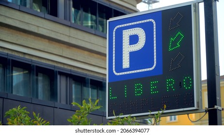 A Blue Road Sign Showing Motorists Where To Park In The City For Their Personal Travel Scenarios. Free Parking. Pointer. Cars And Traffic In The City. Paid Supermarket Parking 