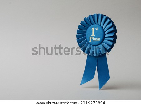 Blue rosette first place on a grey background as a reward for achievement, success and victory.