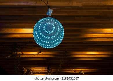 Blue Round Lamp With Flowers Pattern As A Shade Hanging Against Wooden Background