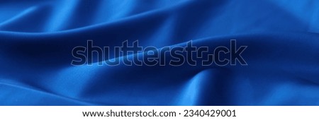 Blue satin background or design element. Waved blue fabric close up.