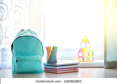 Blue school backpack with school supplies on table over children room interior in sunny day. Back to school concept.