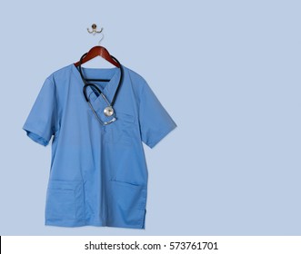 Blue scrubs shirt for medical professional hanging on blue wall