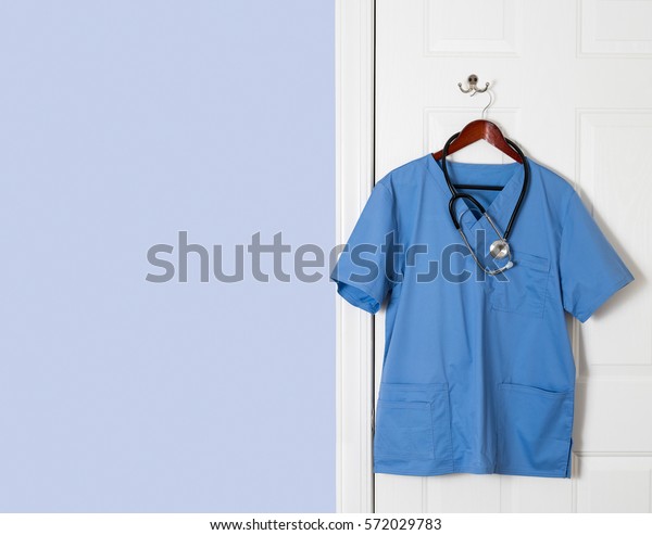 Stock photo of blue medical scrubs on a hanger with a stethoscope hung around the neckline