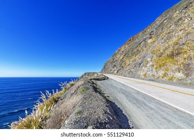 Blue Sea & Sky, White Clouds, Waves Splashing On Huge Rocks, Desolate Road To Nowhere, Along A Rocky Coastline, Traveling The Big Sur Highway (Highway 1) On The California Central Coast.