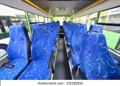 Blue seats for passengers in saloon of empty city bus with grey floor.