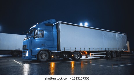 Blue Semi-Truck with Cargo Trailer Drives On Overnight Parking Space where Other Trucks are Standing. Drivers Resting at Night on the Overnight Parking Lot