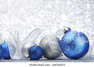 Blue Shiny Christmas Balls And Ribbon On Silver Glitter Stars Background