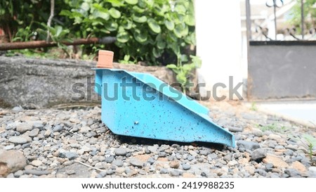 A blue shovel made of plastic for collecting rubbish is on a small rock in front of the house