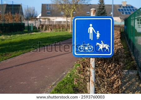 A blue sign indicates a shared path for pedestrians, cyclists, and horse riders along a paved route in a suburban area, promoting safe multi-use access.