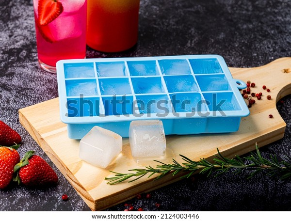Blue silicone ice cube tray on table with fruit and\
strawberry drink