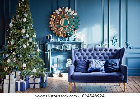 Blue and silver Christmas interior. Living room with blue walls, blue sofa and silver and blue Christmas decorations on Christmas tree
