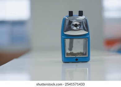 A blue and silver pencil sharpener sits on a white surface. The sharpener has a metal blade frame on top with two black buttons. - Powered by Shutterstock