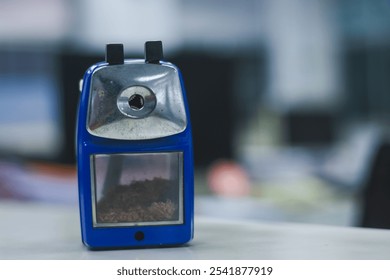 A blue and silver pencil sharpener sits on a white surface. The sharpener has a metal blade frame on top with two black buttons. - Powered by Shutterstock