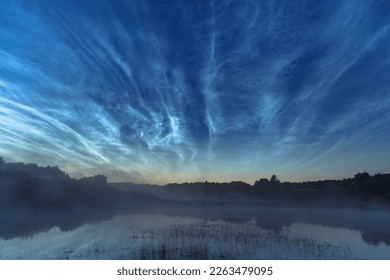 Blue silvery clouds or noctilucent clouds or night shining clouds over water and fog. Noctilucent clouds above the river.