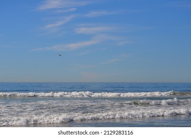 Blue skies with some light clouds above crashing waves along the Cardiff California beach. The horizon is low third allowing copy space in the sky. Contrasting beach crashing waves in the foreground.