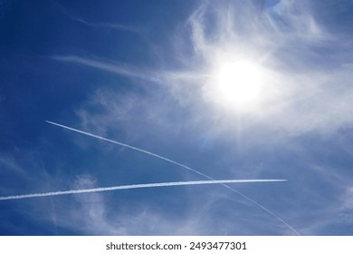 Blue sky background with bright sun and white intersecting airplane steam trails, blue sky crossed by vapor trails from several planes - Powered by Shutterstock