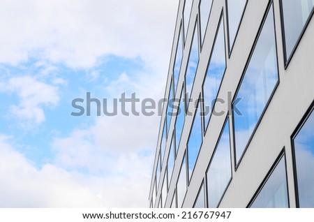 Blue sky and clouds reflected in mirrored windows of new modern building glass facade. Background with free copy-space area for your text.