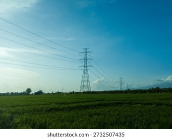 Blue sky with dramatic clouds over the green paddy field and sutet or the extra high voltage transmission line or very high voltage power lines