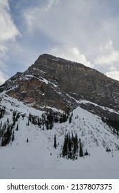 Blue Sky With Few Clouds Above An Arrowhead Mountain With The Base Full Of Snow And The Top Of Solid Rock In Canada