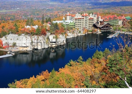 The blue sky and the Mohonk Mountain House resort reflected in Mohonk Lake and surrounded by sandstone cliffs and colorful Autumn trees in the Shawangunk Mountains of New York