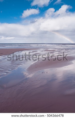 Blue sky and a rainbow over small sandy stream on beach