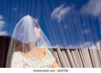 A blue sky with some clouds are reflected off the window of a bridal store.